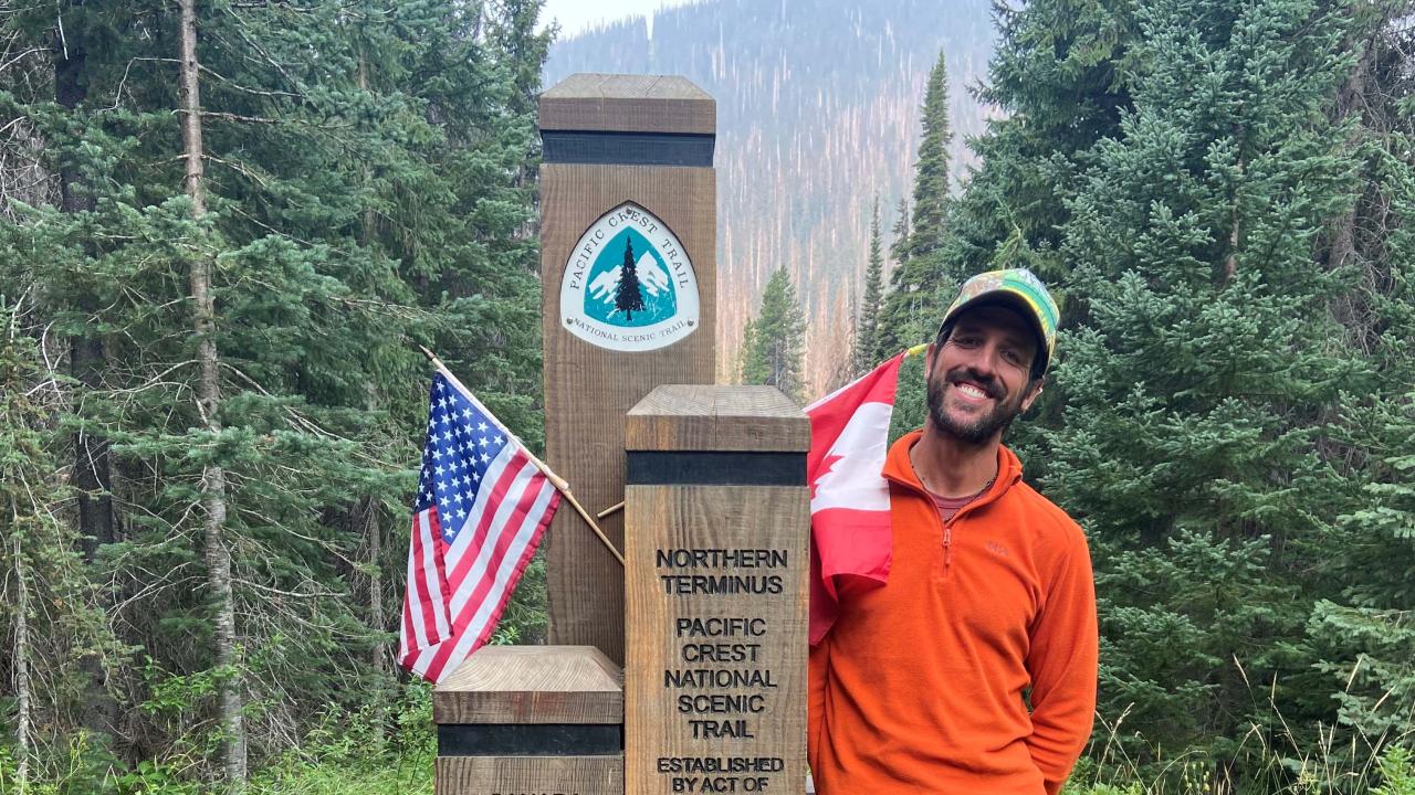 Paul Ronevich standing next to a trail marker on the Pacific Crest Trail.