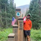 Paul Ronevich standing next to a trail marker on the Pacific Crest Trail.
